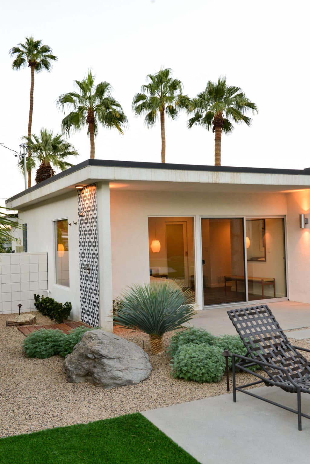 Complete residential landscape design and installation in Palm Springs, including hardscape, custom outdoor shower with tile, fire feature, low voltage lighting, boulders, artificial turf, irrigation and desert plants.